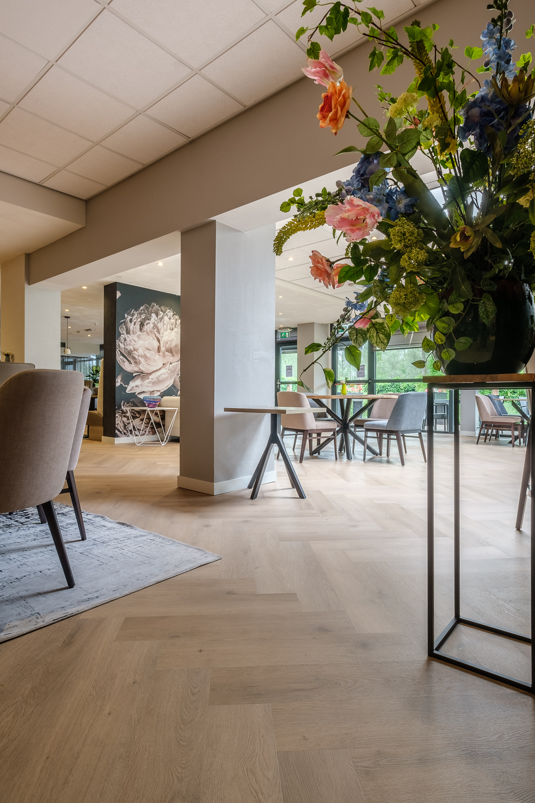 Visgraat PVC vloer in een licht interieur met stoelen, een vloerkleed en een bloemstuk